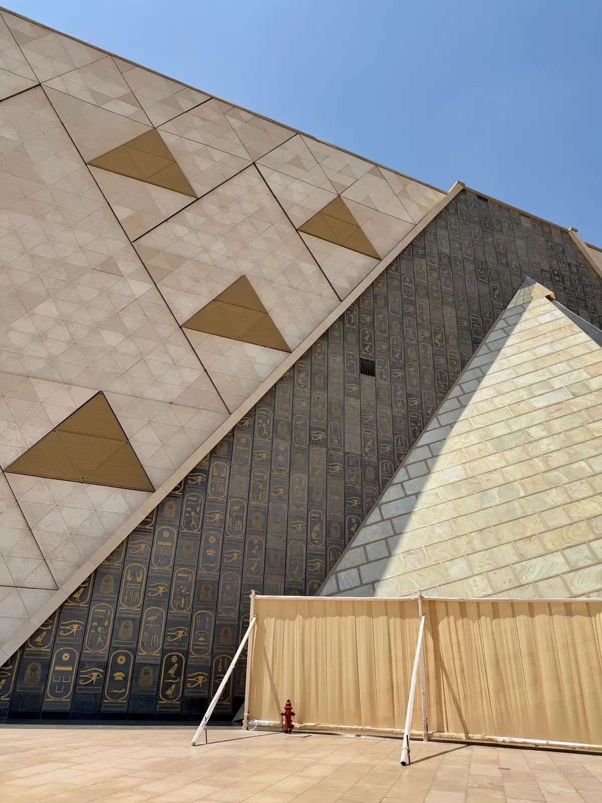 The geometric stone facade of the Grand Egyptian Museum with gilded hieroglyphic panels on a luxury Egypt tour, Grand Egyptian Museum, Giza, Egypt